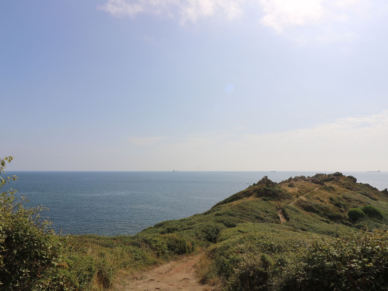A coastal landscape with a dirt path leading to a grassy hill overlooking the sea.