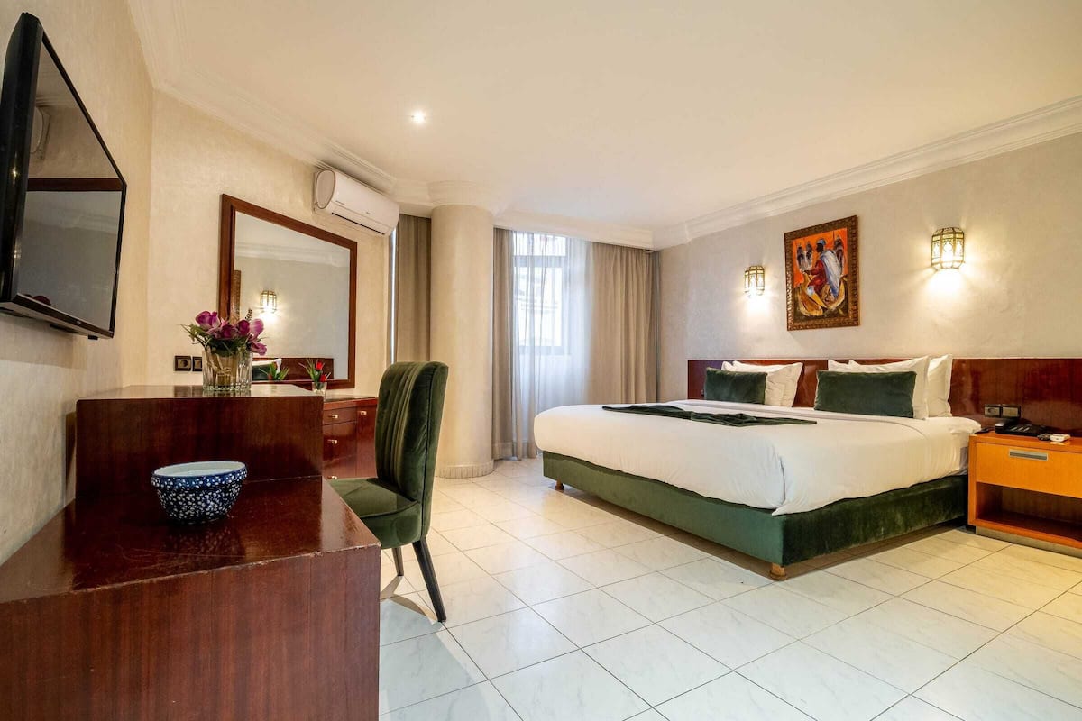Una habitación de hotel con una cama, un escritorio, una silla, un televisor y un cuadro en la pared.