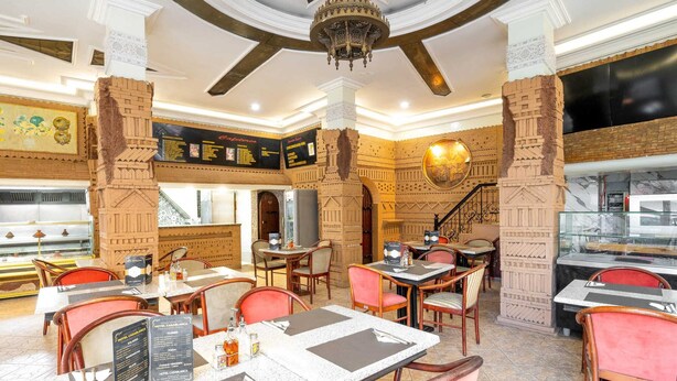 Ein Restaurant mit mehreren Tischen und Stühlen, einer Kandelaber und einer Treppe, die in eine obere Ebene führt.