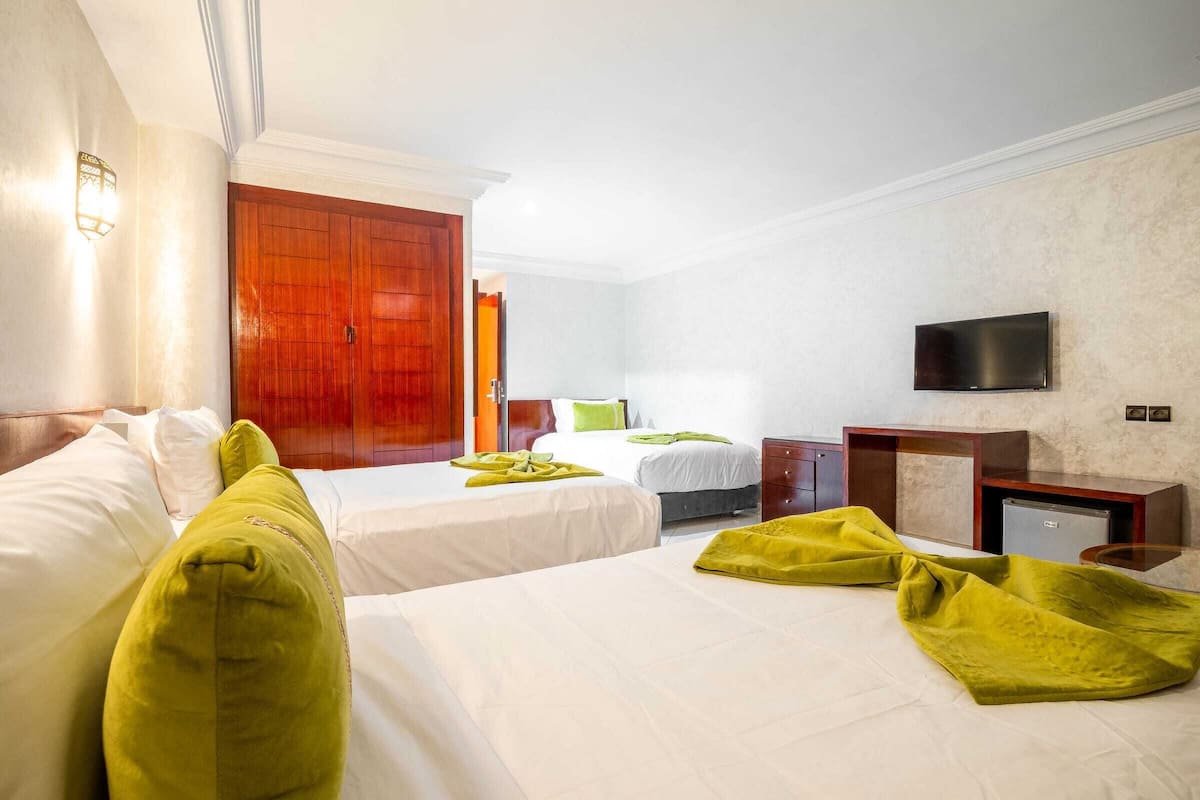 Habitación de hotel con dos camas, televisión, escritorio y armario.