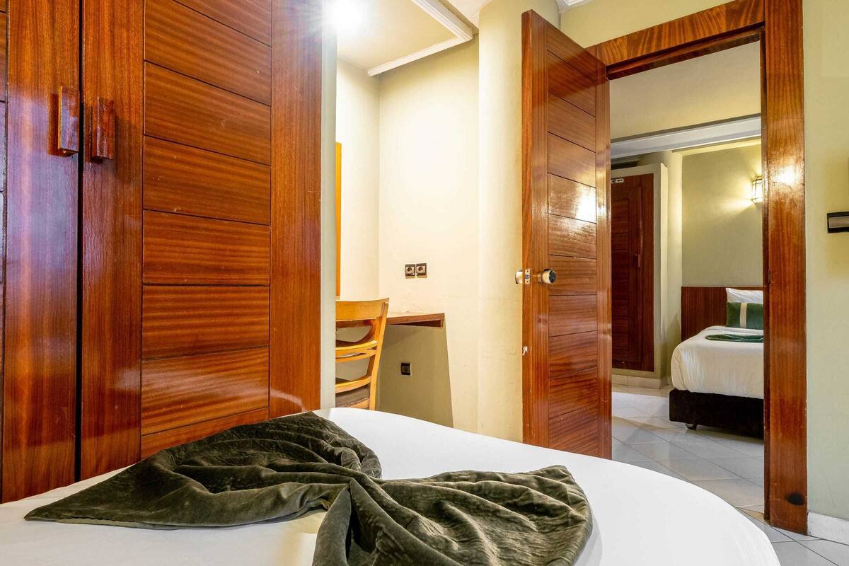 A hotel room with a bed, wooden wardrobe, and a desk with a chair.