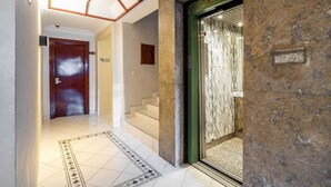 Eine Hotelhalle mit einer Marmortreppe, einer Holztür und einem Aufzug.