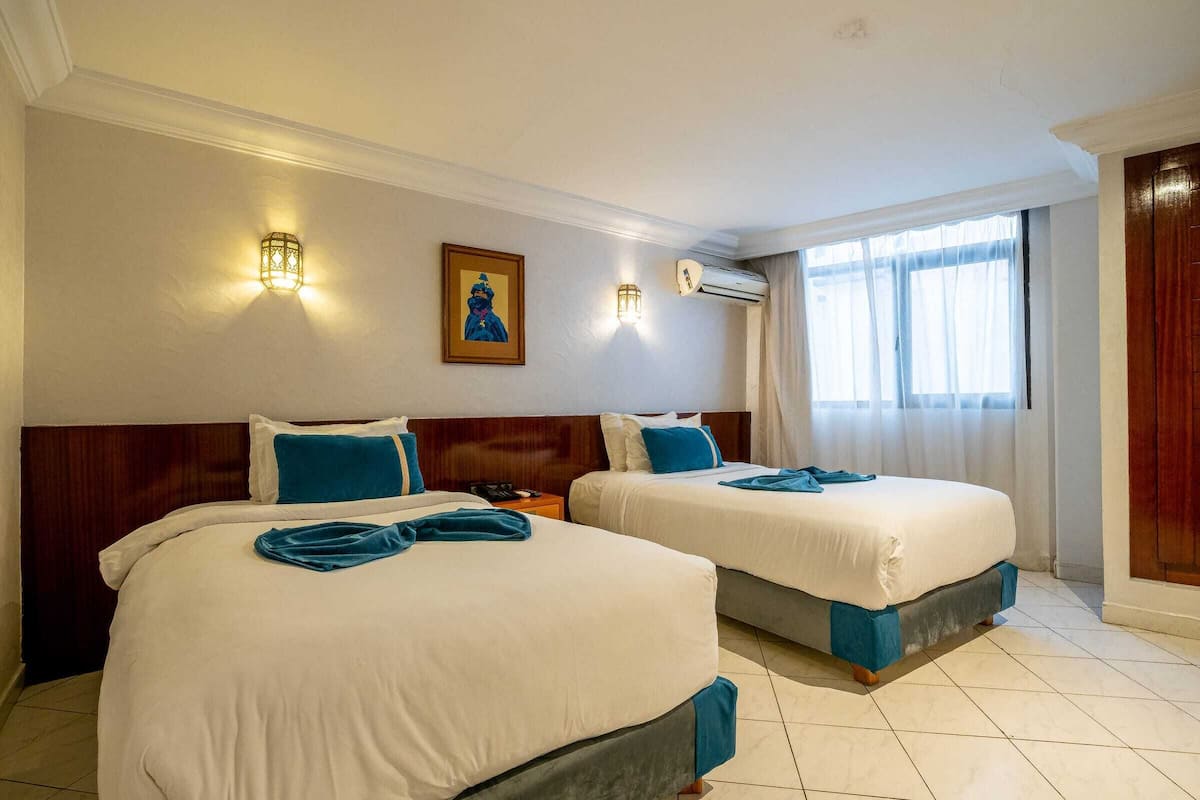 Habitación de hotel con dos camas, cabecero de madera, aire acondicionado montado en la pared y ventana con cortinas.