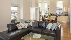 Una sala de estar moderna con un sofá de cuero negro, una mesa de centro de vidrio y un comedor con una mesa y sillas de madera.