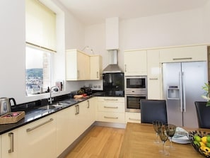 A modern kitchen with a large window, stainless steel appliances, and a dining area with a table set for two. - Apartment 4 Granville Point (Ilfracombe)