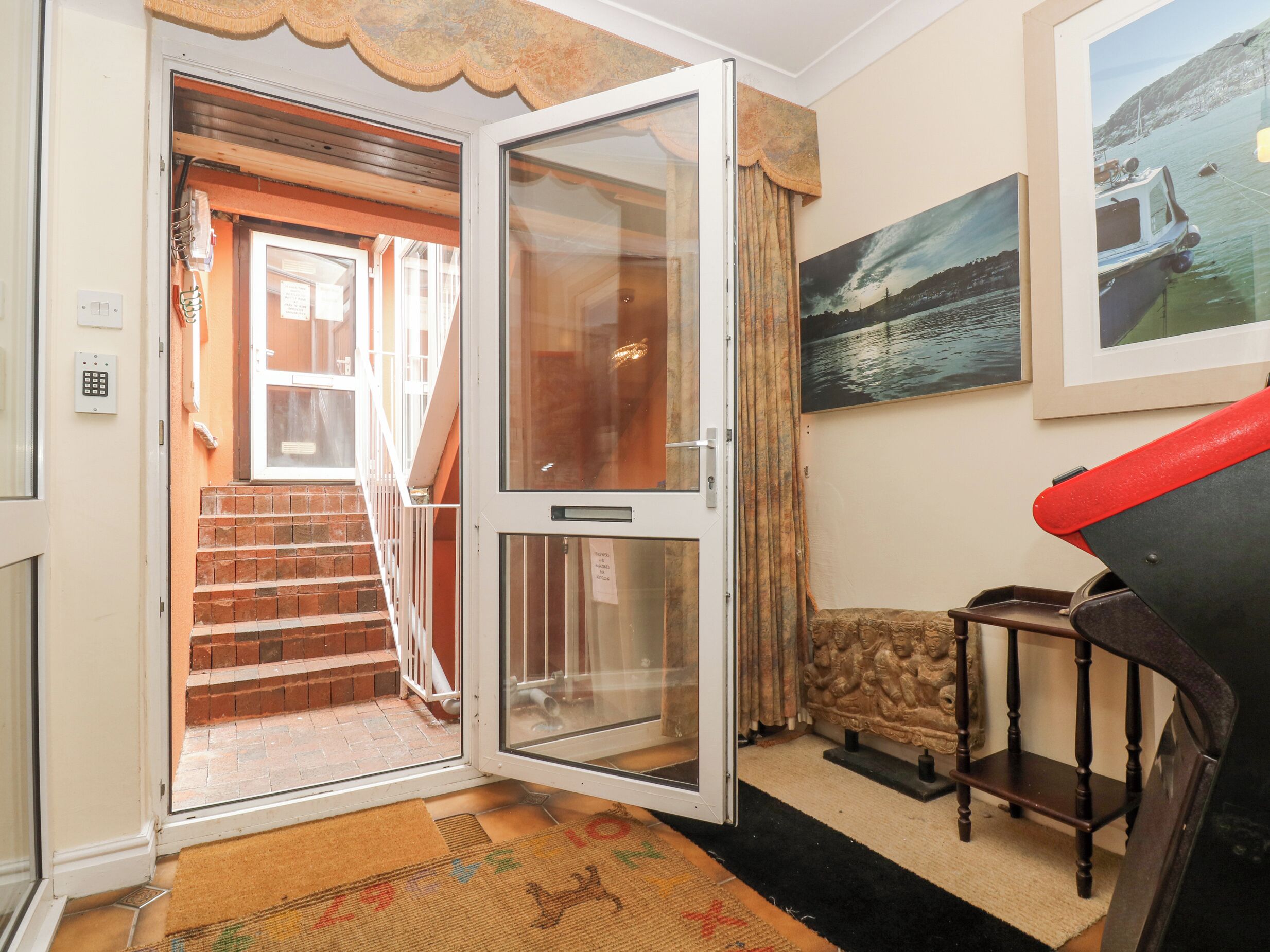 A room with a door leading to a staircase, a framed picture on the wall, and a small wooden table.