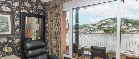 A room with a black leather chair, a framed picture on the wall, and a large window with a view of a harbor and buildings.