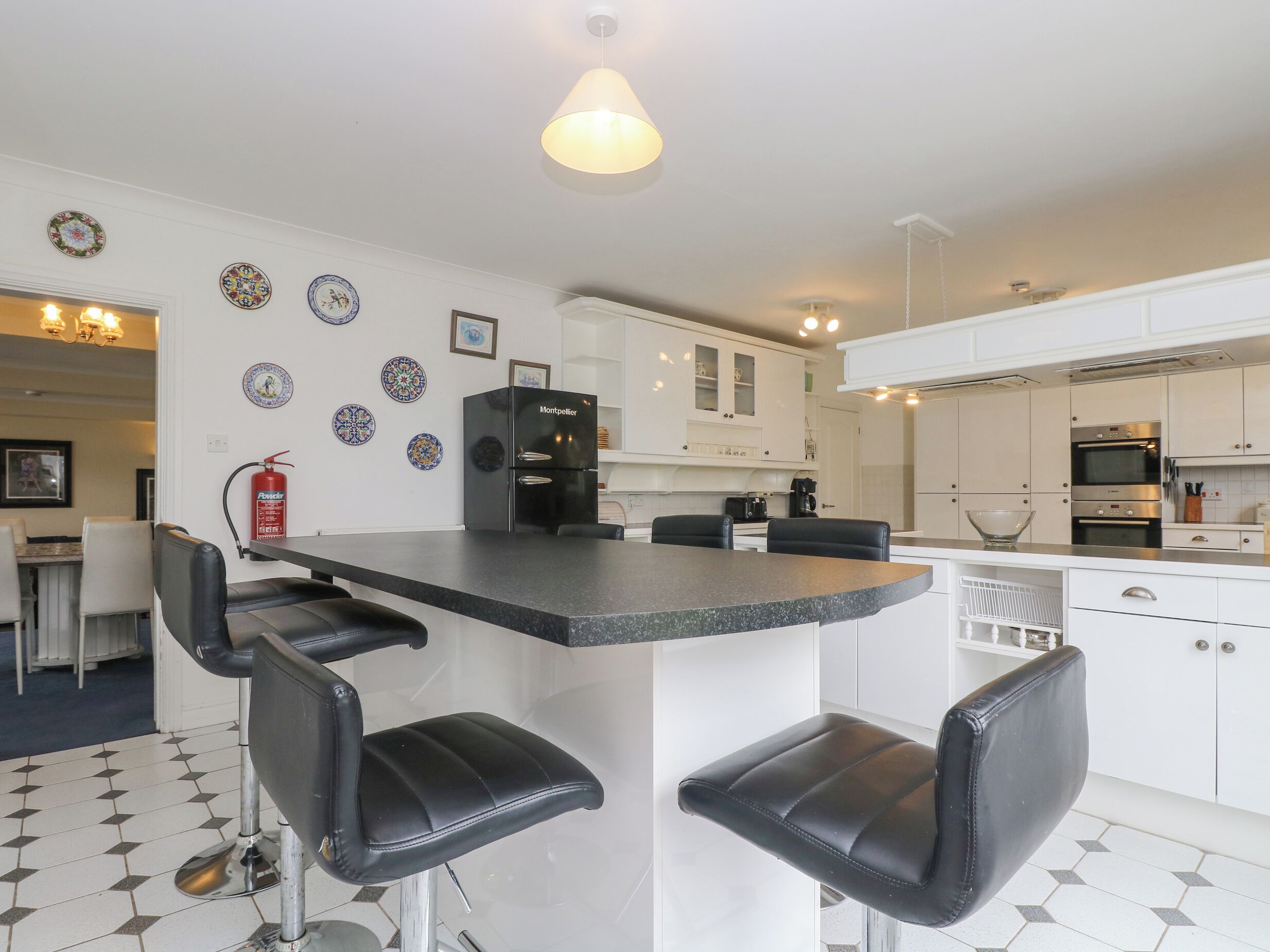 A modern kitchen with a central island, black bar stools, white cabinets, and a black refrigerator.