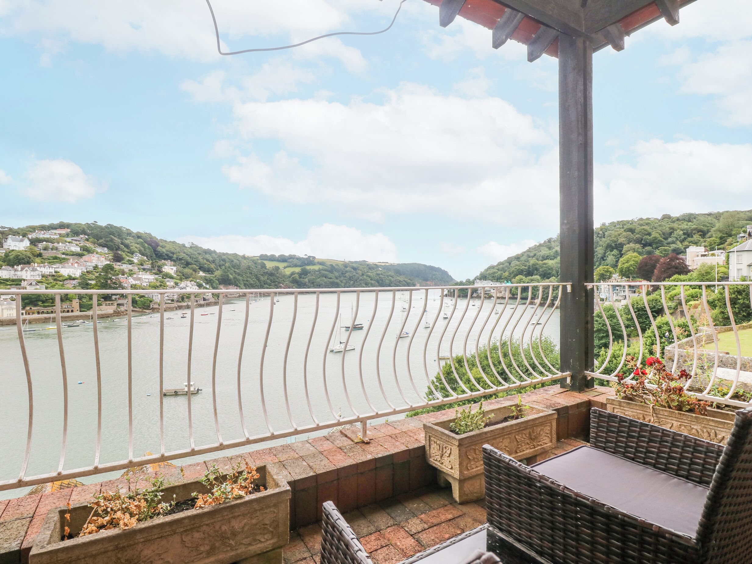A balcony with wicker furniture, a view of a river, and a hillside in the background.