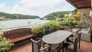 A terrace with a wooden table and chairs, overlooking a bay with boats. - Bight Boathouse (Dartmouth)