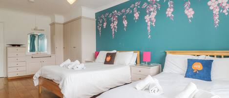 Una habitación de hotel con dos camas, un mural de pared color turquesa, suelo de madera, un aparador blanco y un espejo.