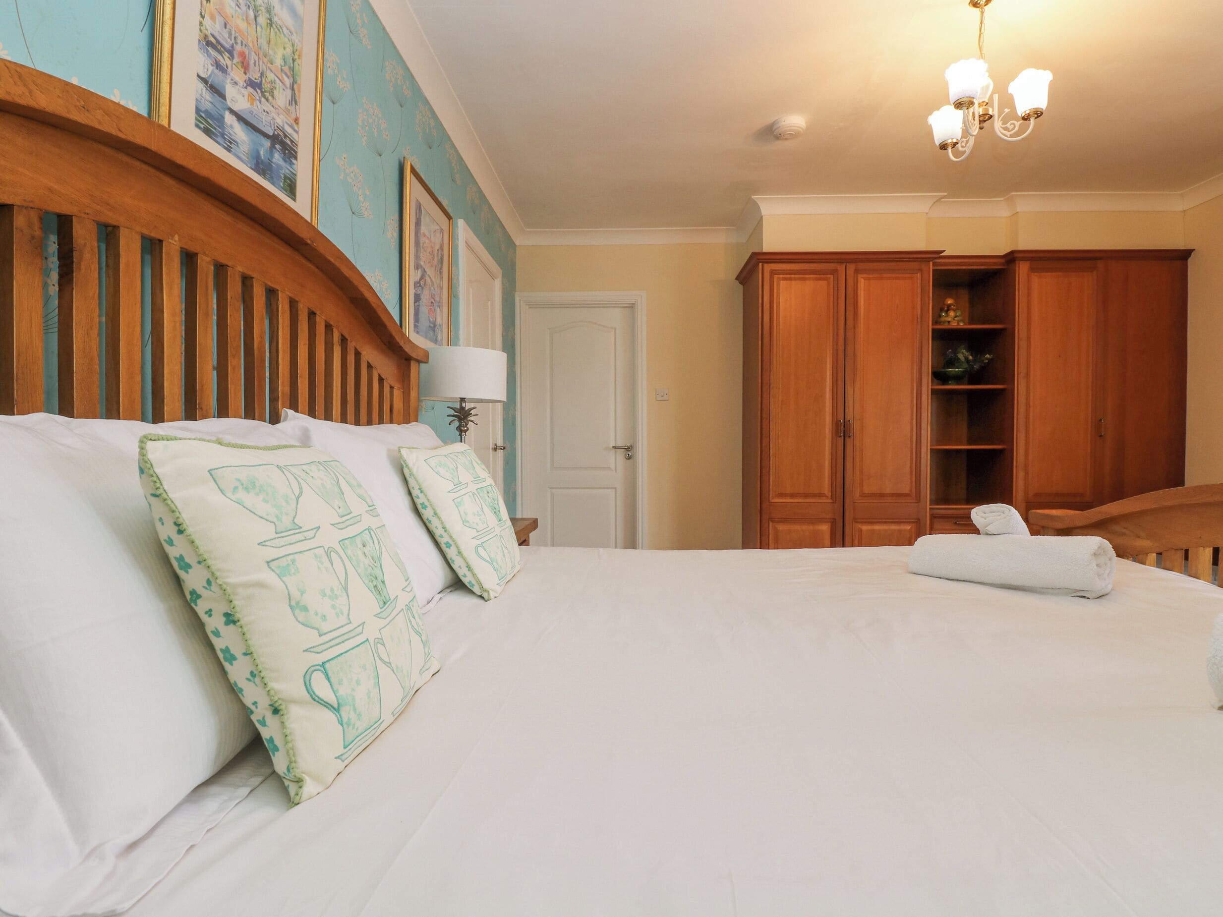 Una cama bien hecha con sábanas blancas y almohadas decorativas, un cabecero de madera, una araña y armarios de madera.