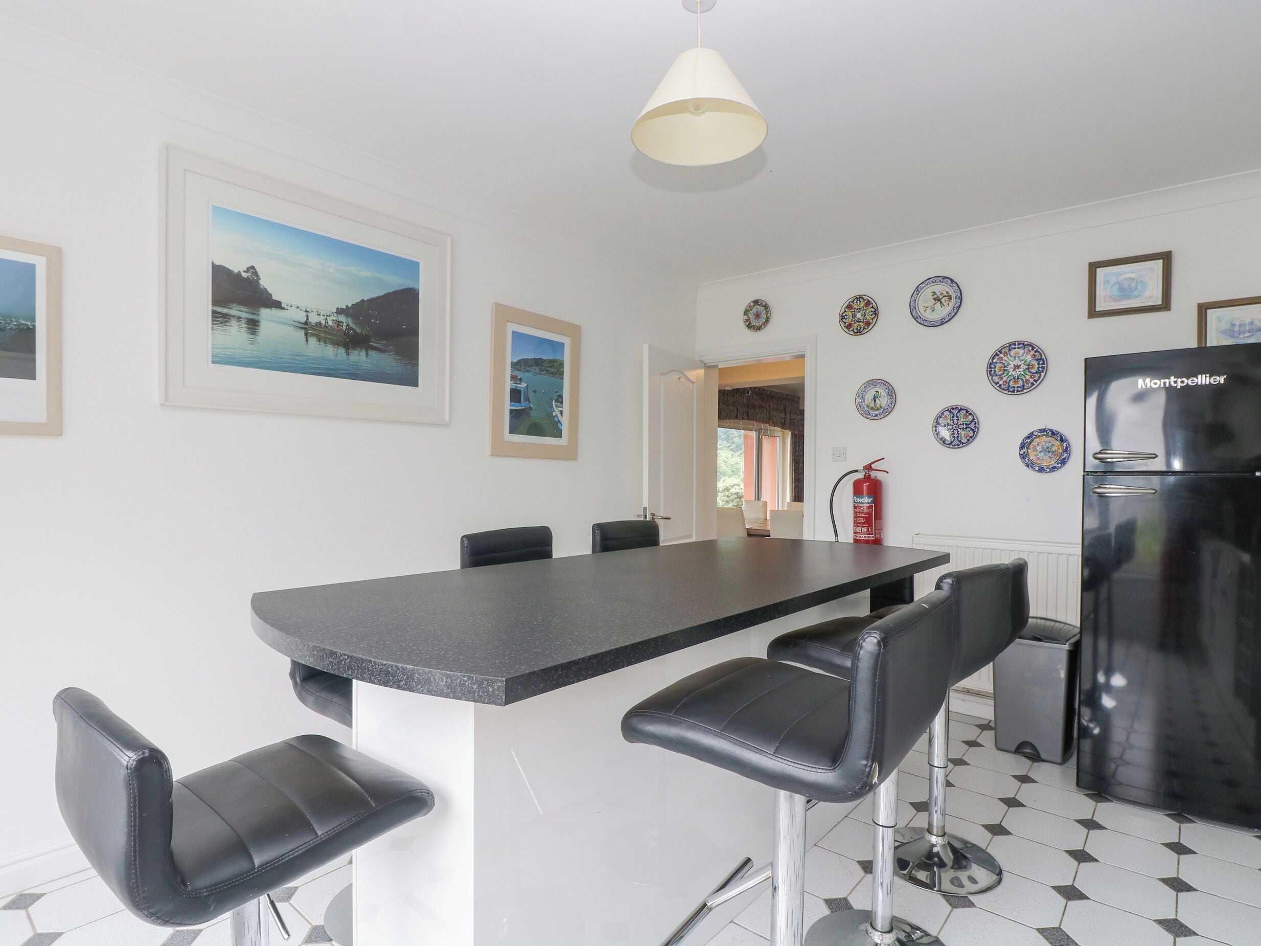 A modern kitchen with a black countertop, black bar stools, a black refrigerator, and decorative plates on the wall.