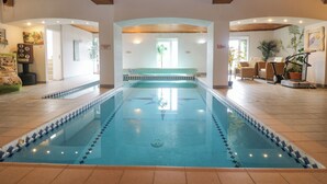 An indoor swimming pool with a tiled floor, wooden ceiling beams, and a seating area with a bench. - Bight Boathouse (Dartmouth)