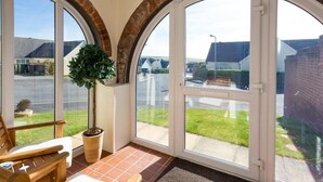 Una veranda con ampie finestre ad arco, una pianta in vaso e una sedia di legno.