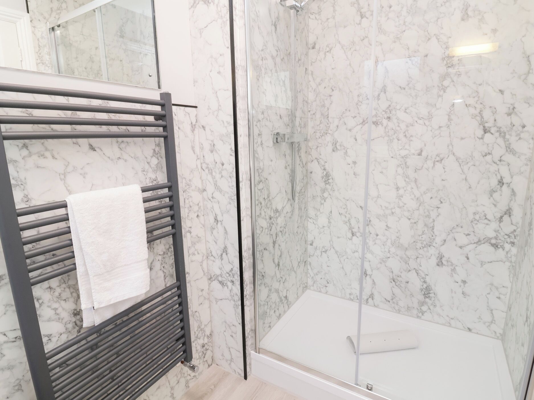 A bathroom with a glass-enclosed shower, a towel rack with a white towel, and marble walls.