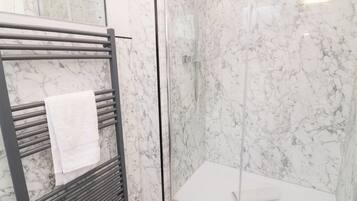 A bathroom with a glass-enclosed shower, a towel rack with a white towel, and marble walls.