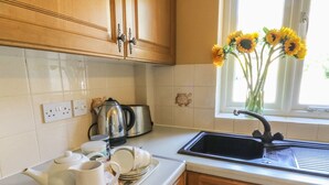 Une cuisine avec des meubles en bois, une bouilloire en acier inoxydable, un grille-pain et une fenêtre donnant sur des tournesols.