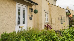 Un bâtiment à deux étages avec une porte et des fenêtres blanches, une enseigne indiquant « Bramble Cottage », et une guirlande verte suspendue.
