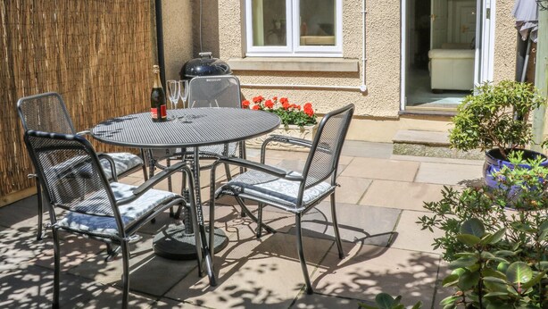 Une terrasse extérieure avec une table ronde et quatre chaises, un barbecue et un pot de fleurs.