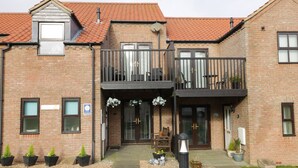 A two-story brick building with a balcony, a door with a glass panel, and potted plants in front. - The Fox's Den (Whitby)
