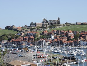 A coastal town with a historic castle on a hill, marina with boats, and traditional red-roofed buildings. - The Fox's Den (Whitby)