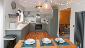 A modern kitchen with a dining table set for two, a hanging light fixture, and string lights. - The Fox's Den (Whitby)