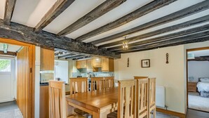 Un grand espace à manger avec une table et des chaises en bois, une cuisine à l’arrière-plan et une vue sur une chambre.