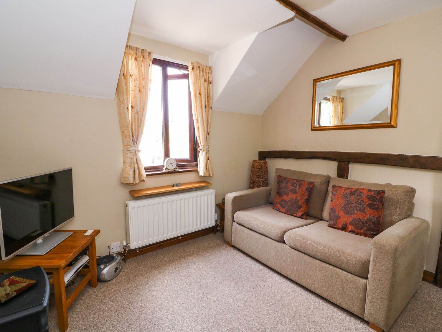 A cozy living room with a sofa, a television, a radiator, and a window with curtains.