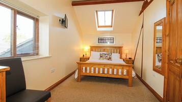 A bedroom with a wooden bed, a chair, a window with blinds, a small skylight, and a door.