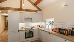 A modern kitchen with white cabinets, a wooden ceiling, and a built-in oven. - Rhianwen, Plas Moelfre Hall Barns (Oswestry)