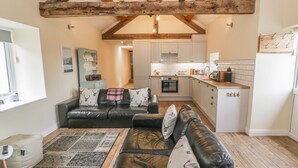 A cozy living room with a black leather sofa, a patterned rug, and a wooden ceiling. - Rhianwen, Plas Moelfre Hall Barns (Oswestry)