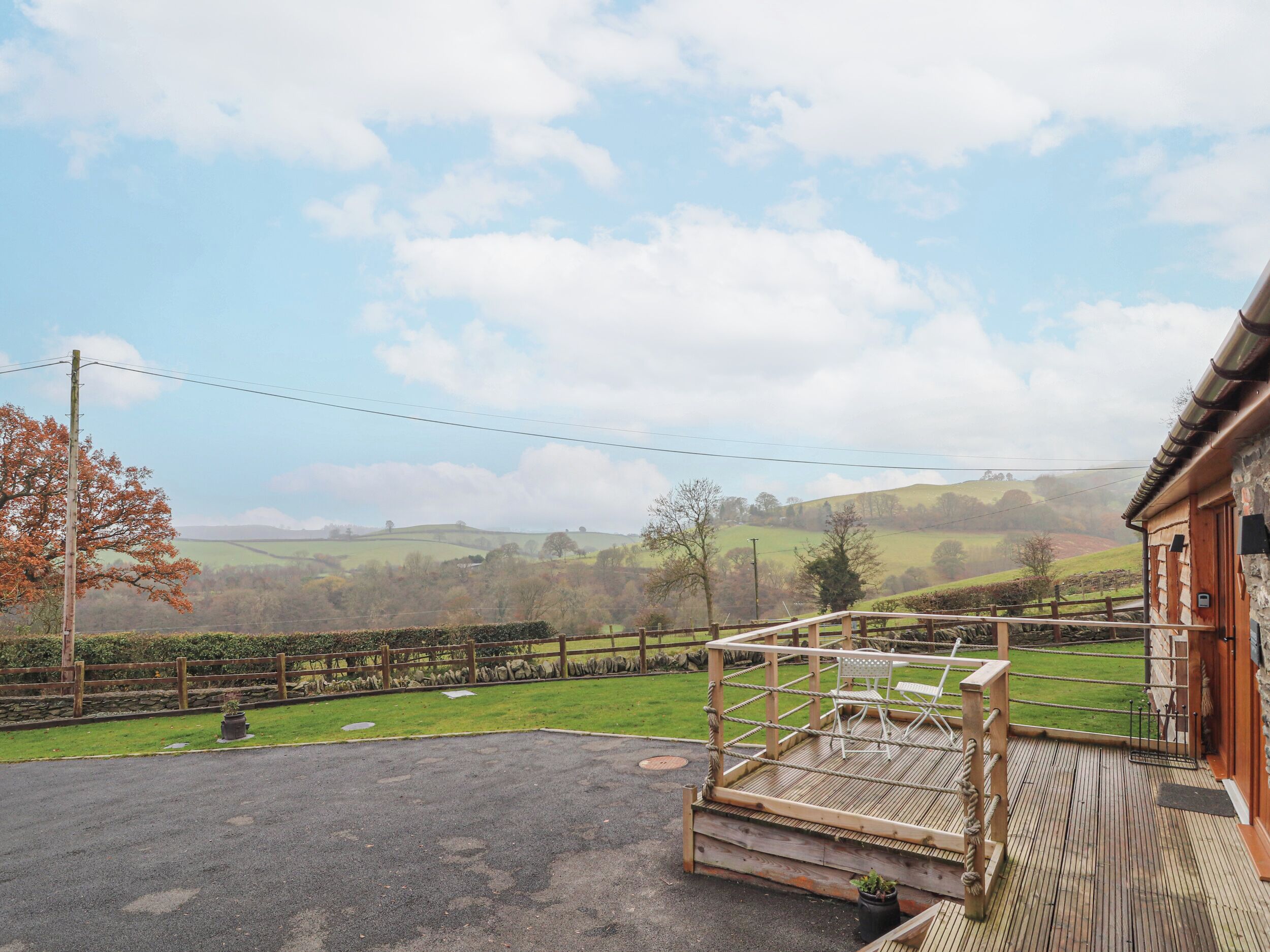 A wooden deck with a rope ladder, a stone wall, and a view of rolling hills in the background.