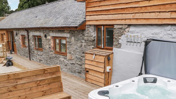 A stone building with wooden steps leading to a wooden deck. A hot tub is visible on the deck. - Rhianwen, Plas Moelfre Hall Barns (Oswestry)