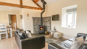 A cozy living room with a stone fireplace, leather sofas, and a dining area with a wooden table and chairs. - Rhianwen, Plas Moelfre Hall Barns (Oswestry)