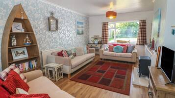 A living room with a sofa, two armchairs, a coffee table, a bookshelf, a television, and a window with curtains.