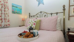 A neatly made bed with floral bedding, a star decoration on the wall, and a bedside table with a lamp and a power outlet. - Salty Puffin (Tyn-y-Gongl)