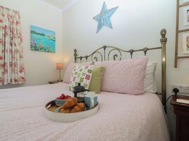 Una cama bien hecha con ropa de cama floral, una decoración de estrella en la pared y una mesita de noche con lámpara y toma de corriente.