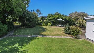 A well-maintained lawn with a patio area, surrounded by dense foliage and a clear sky.