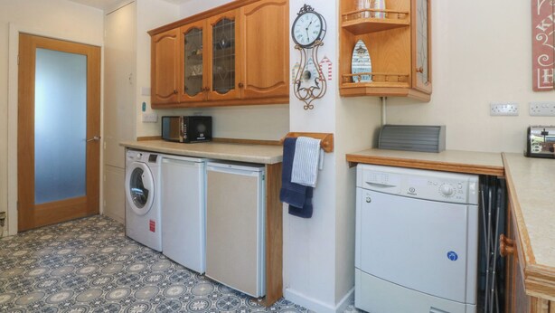 A compact kitchen with a washing machine, a dishwasher, and wooden cabinets. - Salty Puffin (Tyn-y-Gongl)
