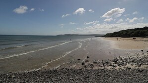 A beach with pebbles, calm water, and a clear sky. - Salty Puffin (Tyn-y-Gongl)