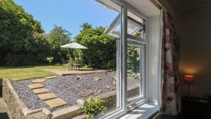 A window with a view of a garden patio area, including a table and chairs, and a small water feature. - Salty Puffin (Tyn-y-Gongl)