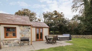 A stone house with a patio, a barbecue, and a hot tub. - Y Beudy Cottage (Caernarfon)