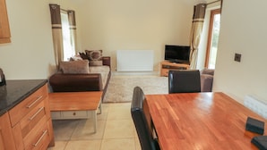 A compact living space with a sofa, a dining table, a TV, and a radiator. - Y Beudy Cottage (Caernarfon)