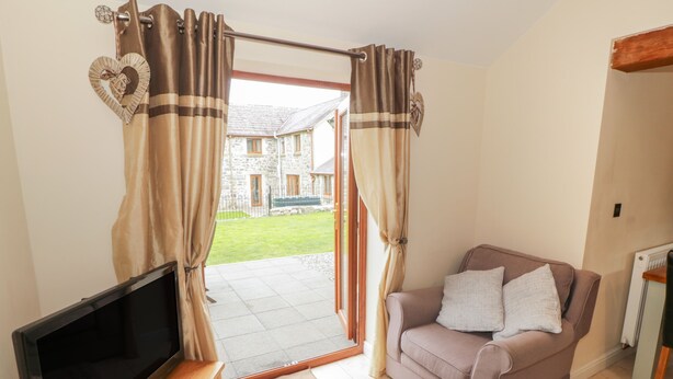 A living room with a flat-screen TV, a sofa, and a large window with curtains. - Y Beudy Cottage (Caernarfon)
