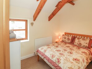 A bedroom with a bed, a window, a radiator, and wooden beams on the ceiling. - Y Beudy Cottage (Caernarfon)