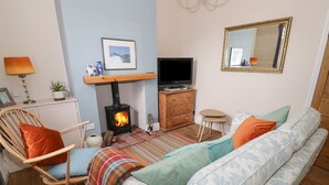 A cozy living room with a wooden sofa, a chair, a TV, a fireplace, and a mirror on the wall. - 24 College Lane (Stratford-upon-Avon)