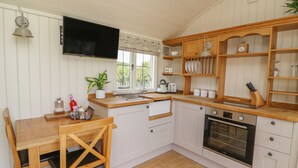 A compact kitchen with white cabinets, a wooden countertop, a built-in oven, and a TV mounted above the counter. - Hillside View (Rhayader)