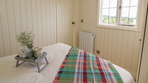 A bedroom with a bed, a window, a radiator, and a small table with a vase of flowers. - Hillside View (Rhayader)