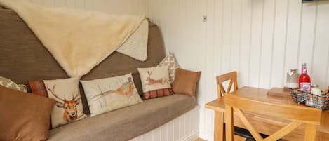 Una habitación acogedora con un banco de madera y una mesa, un televisor en la pared y una ventana con paneles blancos.